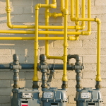 Three gas meters on side of building connected with yellow pipes